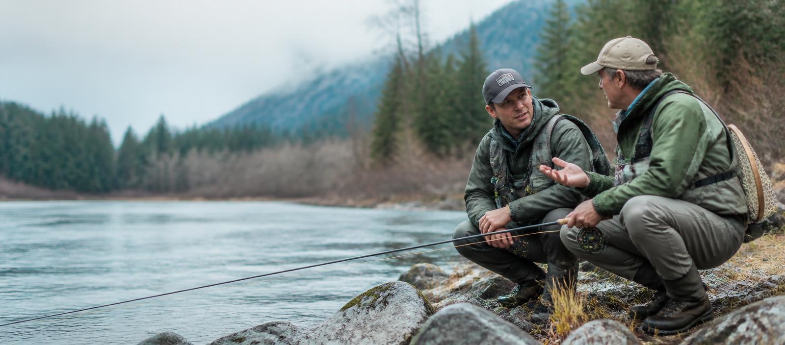 Two anglers crouched on a river bank talking through the plan for the day
